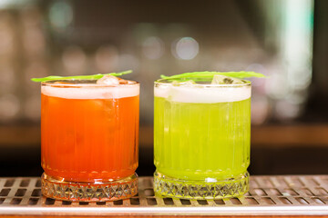 view on glass with red and green drink on bar. Blurred background