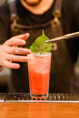 The bartender using tongs decorates a cocktail with a green leaf
