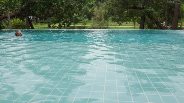 Beautiful long-haired woman swims in an outdoor infinity pool against the backdrop of tropical vegetation, 10 bit prores