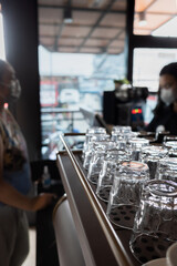 An Array of Clean Glasses in a Coffee Shop with a Cashier Serving a Female Customer on the Background