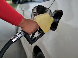 man hand holding a green gas nozzle. A man's hand is pulling the fuel dispenser out of the red...