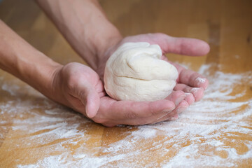 Lump of dough for pizza in the palms in the process of preparing the dough on the wooden table with flour on it