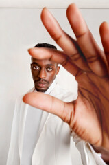African man gesturing and looking at camera. Person dressed in white on white background.