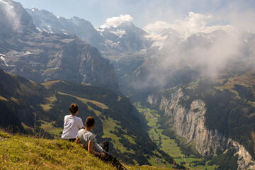 Fototapeta na wymiar Couple of hikers in a valley of the Alps mountains of Switzerland enjoying the panoramic view