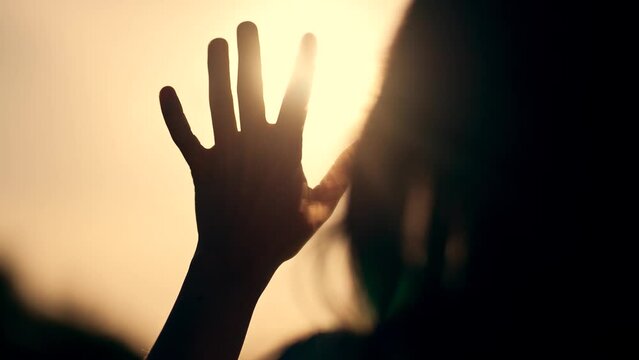 Silhouette of happy dreaming girl pulls her hand to the sun. Religion helping hand. Happy girl pulls her hand. Prayer in religion. Silhouette of hand in the sun. Happy girl silhouette at sunset