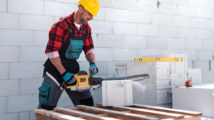 A bricklayer saws an aerated concrete block with a special saw.