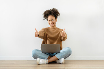 Black girl student with a laptop pointing fingers up against the background of a white wall, panorama