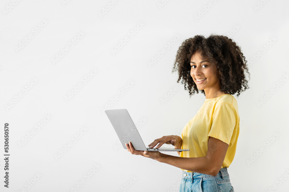 Wall mural cheerful black woman holding a laptop in her hands and pressing her finger on the keyboard while wor