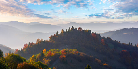 forested rolling hills in evening light. mountain ridge in the distance. beautiful landscape in autumn