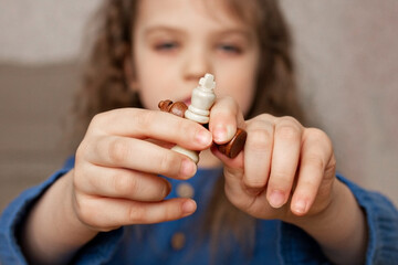 two white and brow wooden chess queen in finger of little girl, close-up, selective focus, games for children, learning chess game, leisure