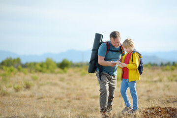 Cute schoolchild and mature father hiking together on mountain and exploring nature. Child learning survival skills and orienteering. Concepts of adventure, scouting and hiking tourism for kids.