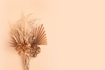Bouquet of beige dried flowers, grass and leaves on beige background top view