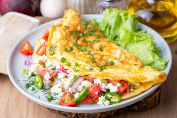 Homemade stuffed omelet on a plate. Egg omelet stuffed with fresh tomatoes, cheese and green parsley. Healthy vegetarian breakfast recipe.