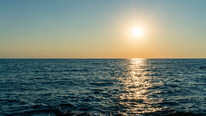 Obraz premium Beautiful sunset behind the blue ocean with small waves