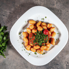 Gnocchi in sugo sauce with some parsley served in white plate on burnt cement table with pieces of tomato and parsley scattered on the table, Top view