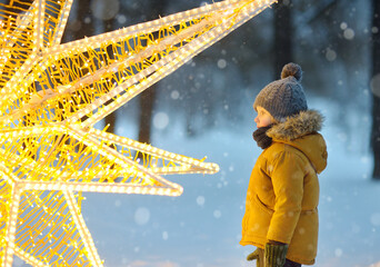 Little boy is admiring a large glowing street decoration in the form of a Christmas star....