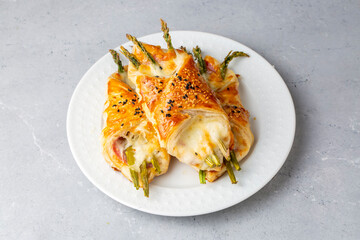 Baked green asparagus with ham and cheese in puff pastry sprinkled with sesame seeds and green basil leaves.