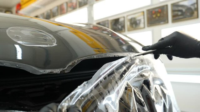 Close up to PPF installation process on a front headlight and hood. PPF is a Paint Protection Film which protect paint from scratches and stone chips. Concept of: Guard, Protect, Car, New, Work.