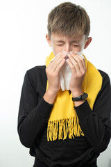 A boy wrapped in a scarf has a runny nose and blows his nose into a napkin.