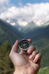 Magnetic compass in the palm of a male hand against the backdrop of a mountain range in the clouds in the summer outdoors, travel, first-person view © yanik88