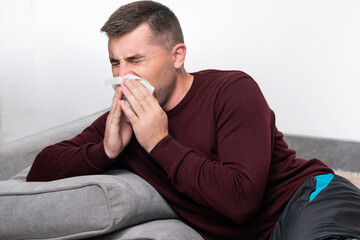 A weak and tired man blows his nose into a handkerchief.