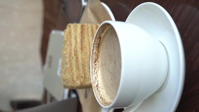Vertical video. Business coffee break, sweet treats, morning at the workplace in a cafe. A cup of coffee with a piece of shortbread cake and a laptop on the table. High quality FullHD footage