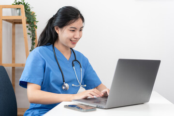 Veterinarian woman in blue uniform is using laptop to searching pet information and typing treatment