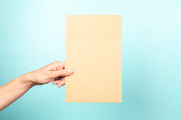 Woman hand holding blank rectangular sheet of brown cardboard on light blue background