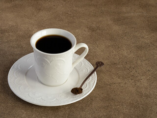 White cup on a saucer of caffein free barley coffee on brown background. Vintage coffee spoon with...