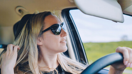 Fototapeta na wymiar A young woman in a good mood behind the wheel of a car.