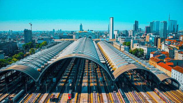 Aerial view of the station where trains arrive. An old arched structure made of metal and glass above the station poles. Tourism. Transport. Skyline with tall buildings. Italy, Milan, 09.2022