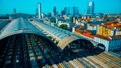 Aerial view of the station where trains arrive. An old arched structure made of metal and glass above the station poles. Tourism. Transport. Skyline with tall buildings. Italy, Milan, 09.2022