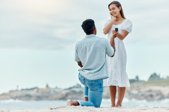 Beach proposal, engagement and surprise woman for love, care and relationship commitment together. Young, engaged and happy marry me couple, summer seaside date and special romance marriage outdoors