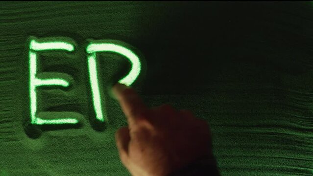Hand drawing the Word Erase in the Green Sand and then erases it. Male hand writes the word Erase on the green sand with green backlight. Top view 4k resolution