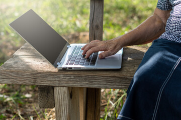 Hands of an older woman using a laptop on the bench, in a park