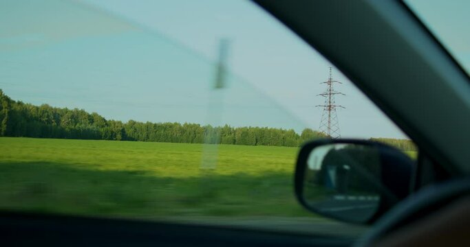 Sunny summer day, a view of a dense forest, a green sunny meadow from the car window, a view through the side glass.