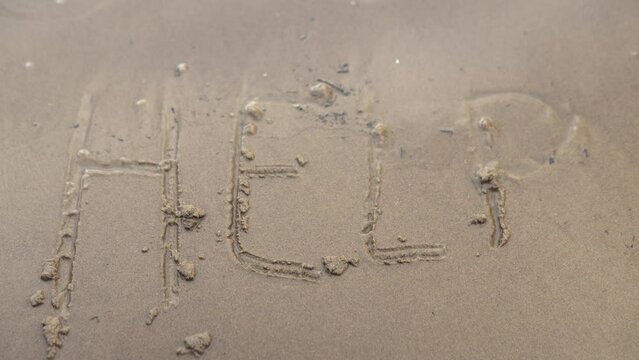 The inscription Help on wet sand on the beach. Waves of water wash off the word close -up.