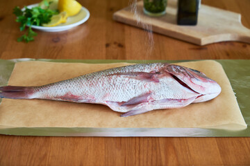 Process of cooking Dorado fish with olive oil and herbs. Female hands close-up.