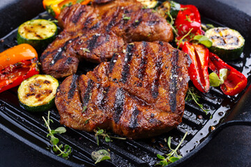 Traditional barbecue pork neck steak with grilled vegetable served and spices as close-up in a rustic design frying pan