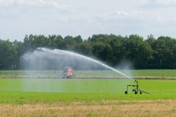 Agricultural sprinkler in the countryside. Field irrigation system. Irrigation hose cart in the background	