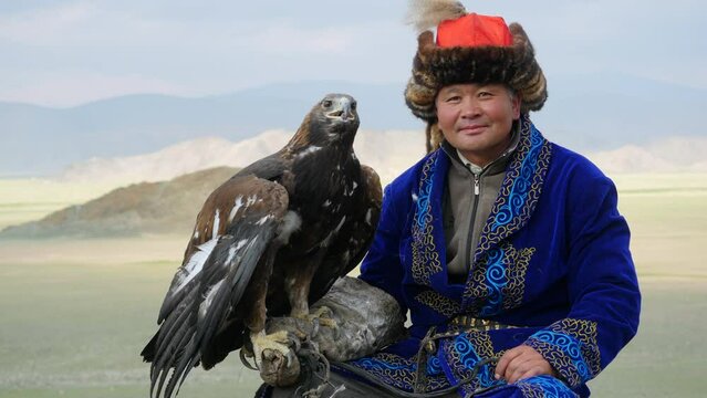 Kazakh Eagle Hunter in traditional clothing holding a golden eagle on his arm near Bayan-Olgii in West Mongolia.