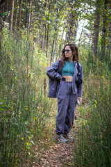 Naklejka na ściany i meble Portrait of romantic woman at fairy forest. A beautiful young girl with glasses is walking through the forest. Girl purple suit. Corduroy fabric