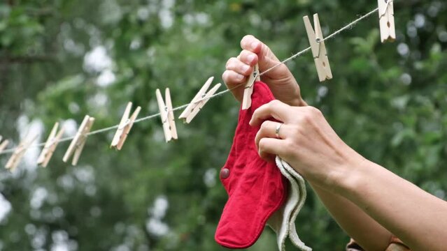 Woman hands hang reusable cloth sanitary menstrual pads to dry on clothesline in the garden. Zero waste period. Feminine washable, eco friendly personal hygiene supplies. Womens health care. 