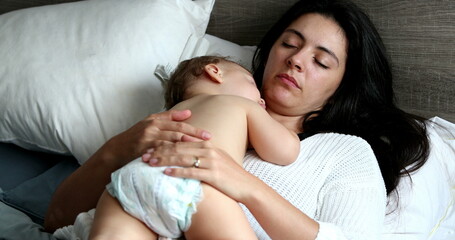 Obraz na płótnie Canvas Casual mother and baby napping lying in bed. Infant child asleep on parent chest sleeping
