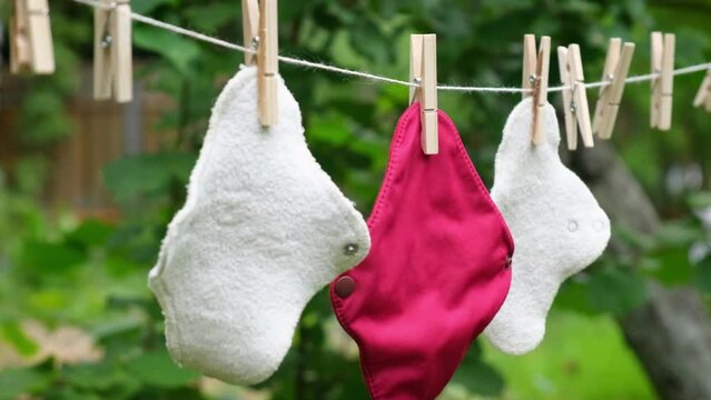 Three reusable cloth sanitary menstrual pads hanging to dry on clothesline in the garden. Zero waste period. Feminine washable, eco friendly personal hygiene supplies. Womens health care. Sustainable 