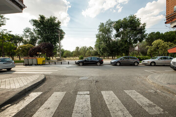 Fototapeta na wymiar narrow city street with sidewalks, zebra crossings and access to a tree-lined park