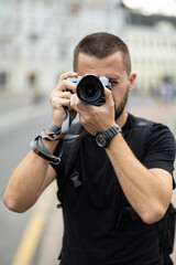 Portrait of young adult caucasian photographer taking a picture with a retro style camera against blurred city at background