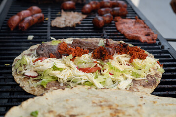 top view of Mexican food Tlayuda de cecina y chorizo and its preparation ingredients on a wooden table, frijoles, beans, cecina, sausage, lettuce, sauce, fruit water