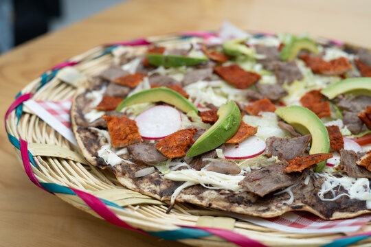 top view of Mexican food Tlayuda de cecina y chorizo and its preparation ingredients on a wooden table, frijoles, beans, cecina, sausage, lettuce, sauce, fruit water