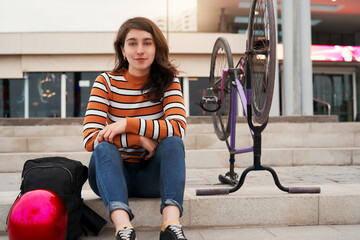 young latin female cyclist sitting relaxed on steps outdoors smiling portrait